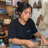 Woman in black Calma t-shirt working with woven material at craft table in studio workshop