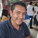 Smiling man wearing dark polo shirt at an outdoor gathering with other people in the background