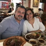 A man and woman smile at the camera at a restaurant table with Mexican food dishes in front of them