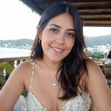 Woman with long dark hair smiling at camera on a terrace overlooking a coastal town and bay