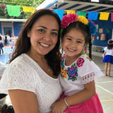 Woman and young girl smiling at school event wearing colorful flower headpieces and festive outfits